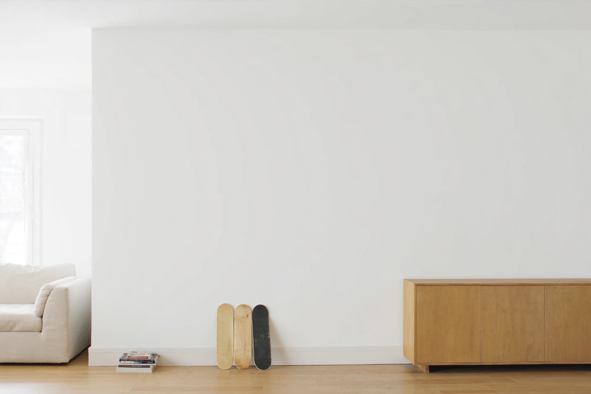 Trois planches de skateboard posées contre un mur blanc dans un salon lumineux au parquet en chêne