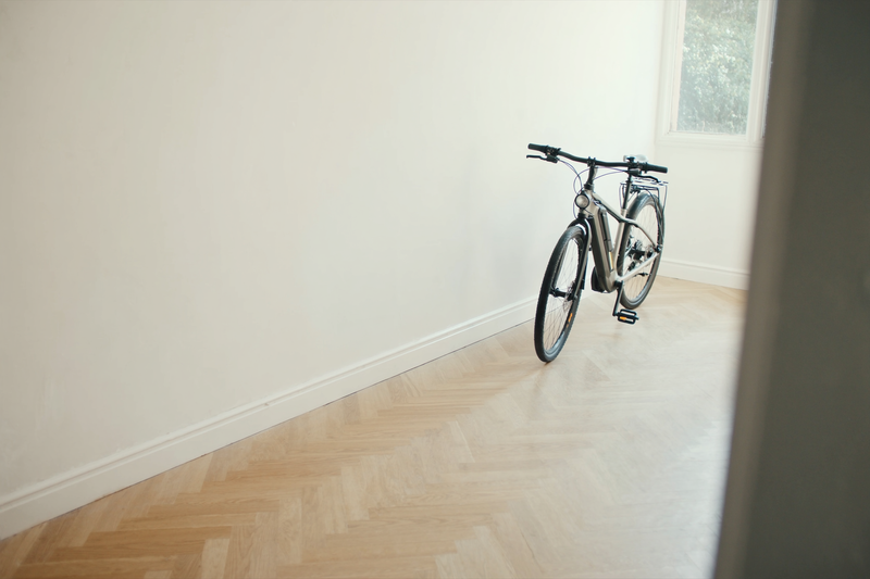 Vélo électrique de ville posé contre le mur d'une entrée lumineuse au parquet en chêne