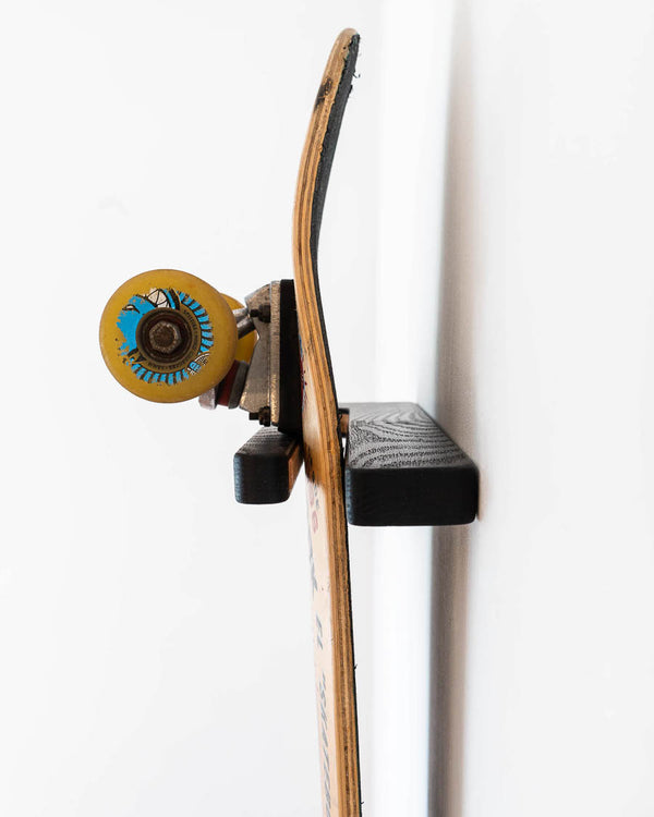 Rack and Ride black-tinted oak vertical skateboard wall mount holding a deck graphic-out