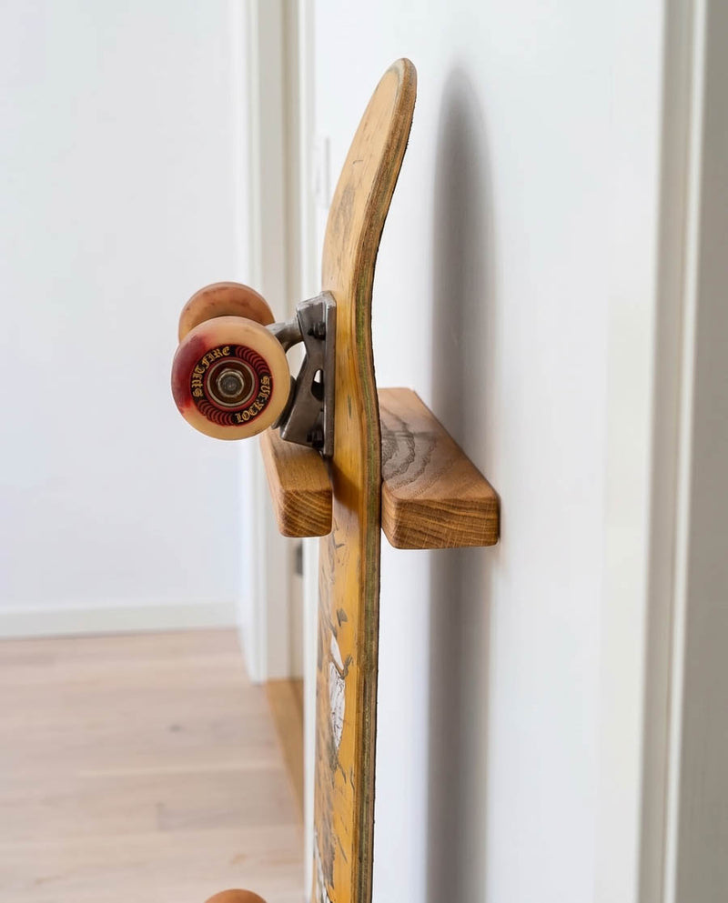 Rack and Ride vertical skateboard wall mount in solid oak holding a deck graphic-out