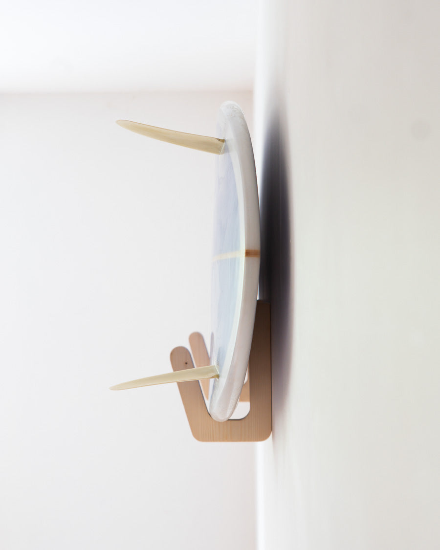 Plywood surfboard wall bracket holding a surfboard flush against a white wall