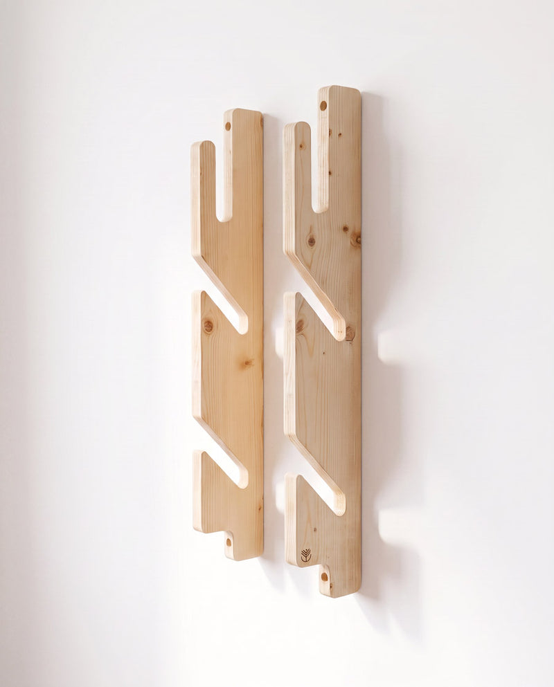Spruce 3-ply triple boardsport rack mounted empty on a white wall, its two notched rails seen from the front