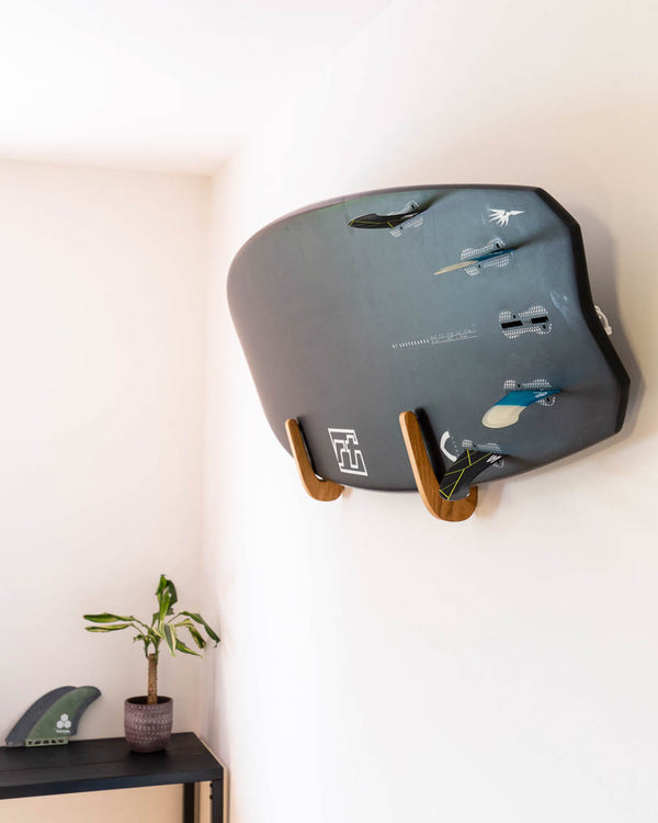 Surfboard displayed horizontally on an oak wall rack with cork-lined cradles