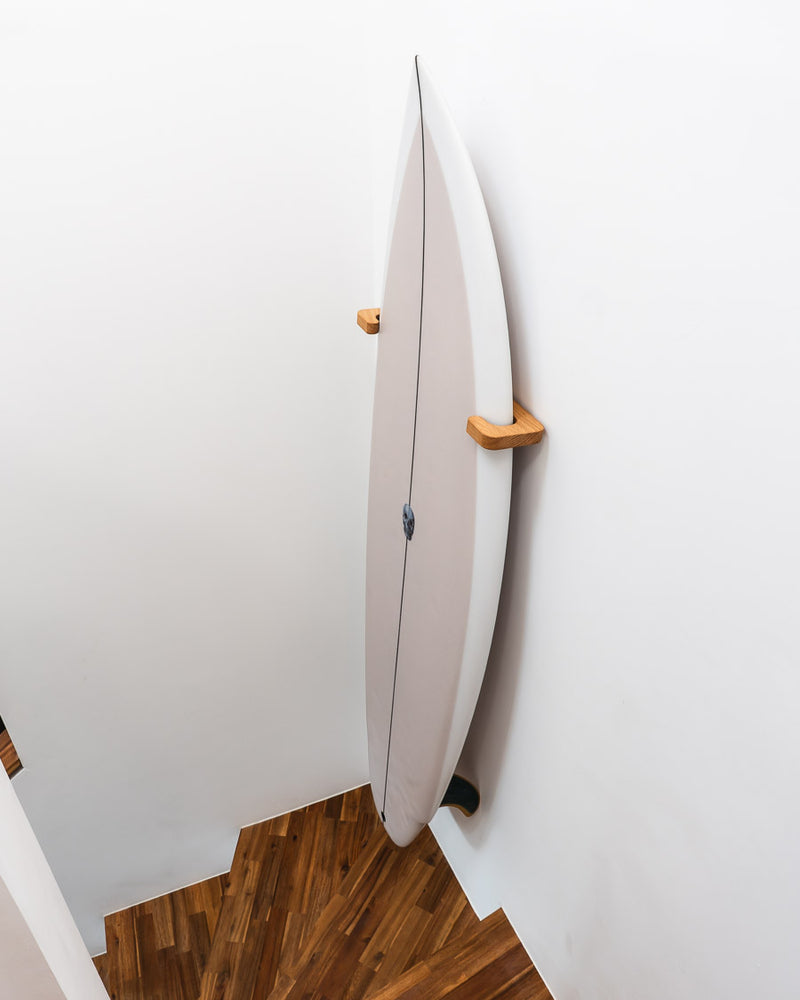 Surfboard senkrecht an einer Eichen-Wandhalterung in einem Treppenhaus aufbewahrt